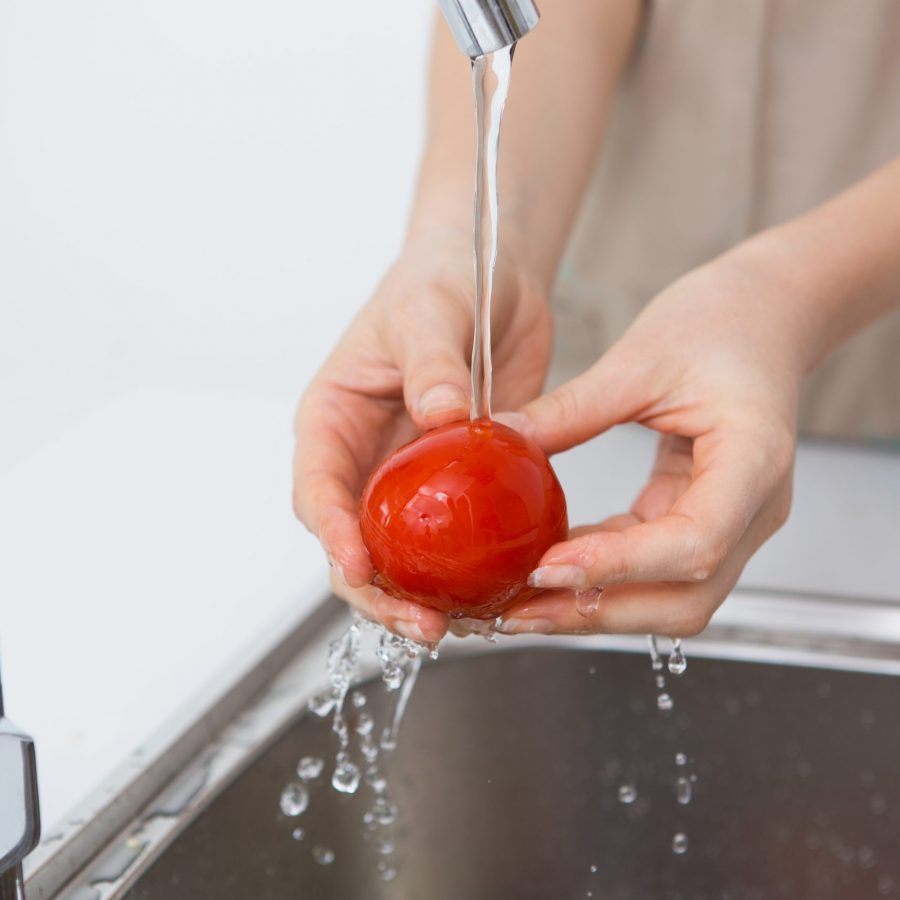 Woman washing tomato with tap water Close-up of unrecognizable woman washing tomato with tap water while preparing vegetable for cooking. Washing product before eating concept