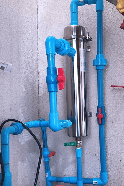Stainless-steel whole-house water filter connected to blue water pipes